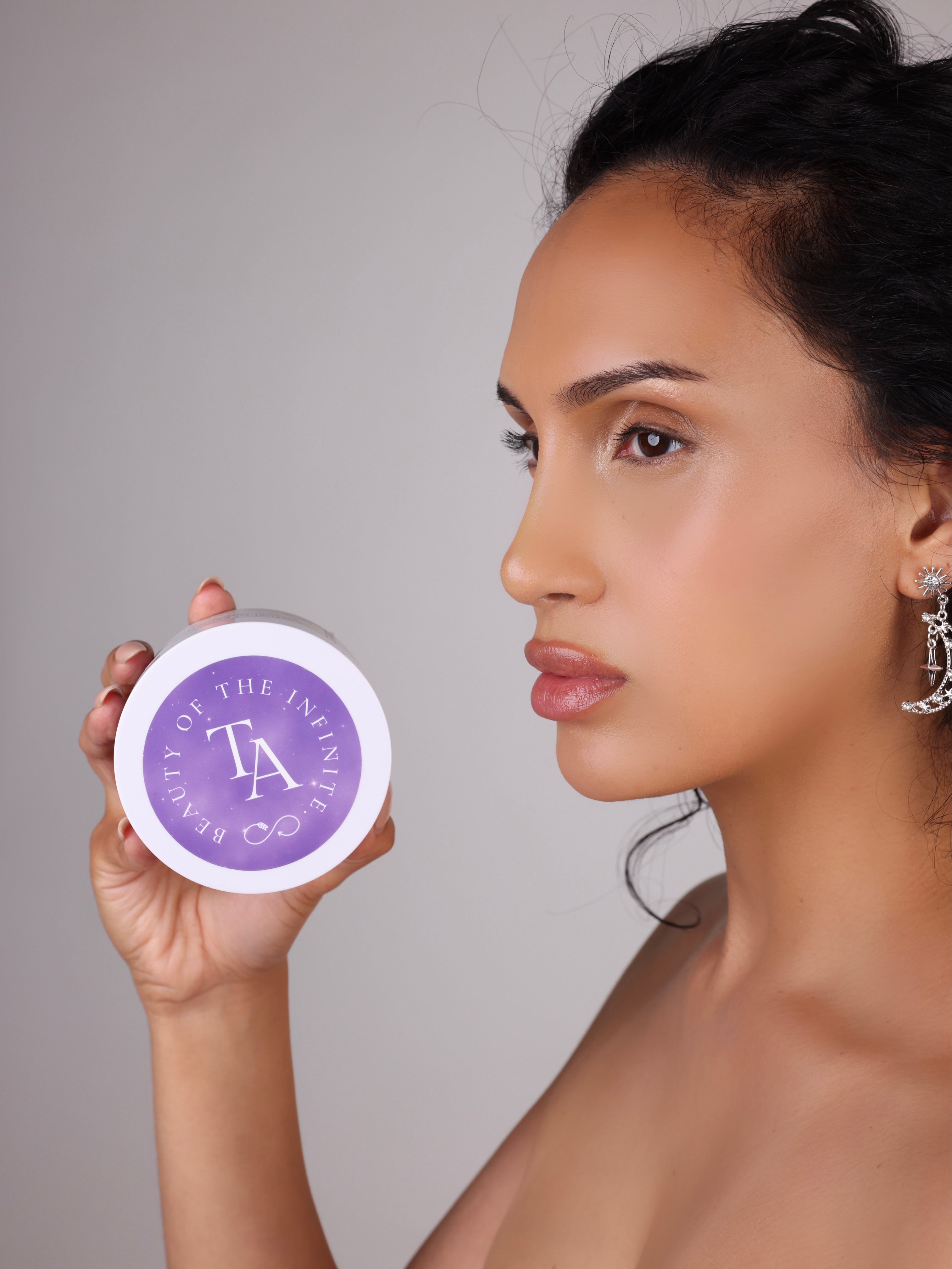 Woman holding a purple container with The Arcturian Lavender Whipped Scrub   logo against a neutral background